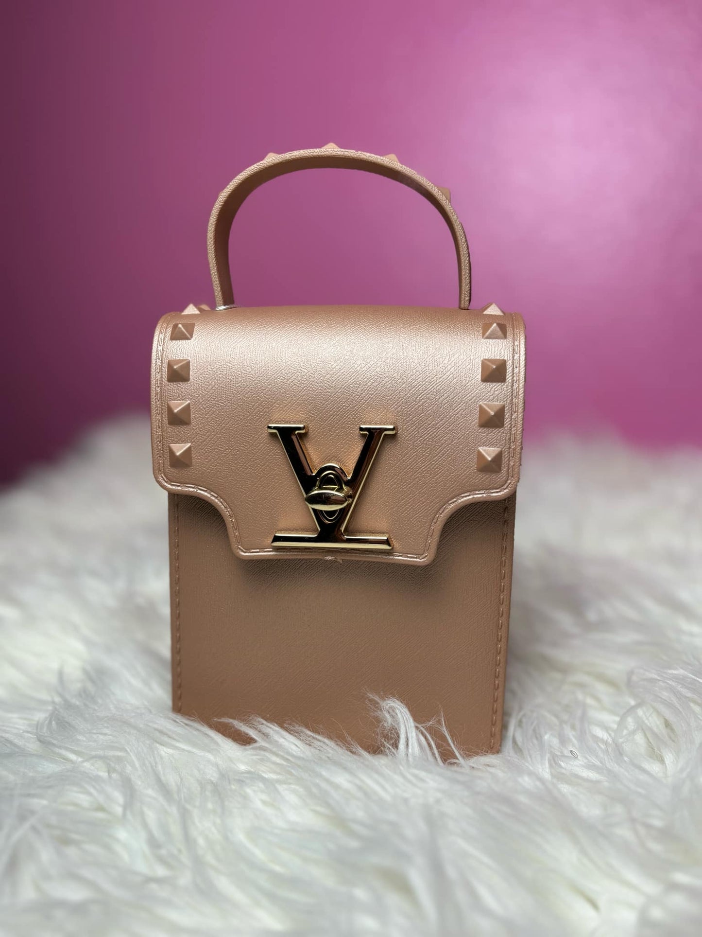 rose gold handbag with studded details on a white surface with a pink background