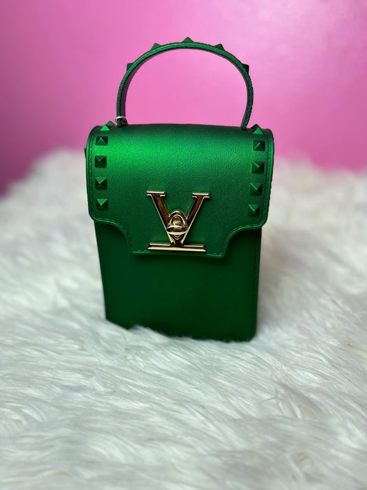 Green handbag with gold accents on a white surface with pink background